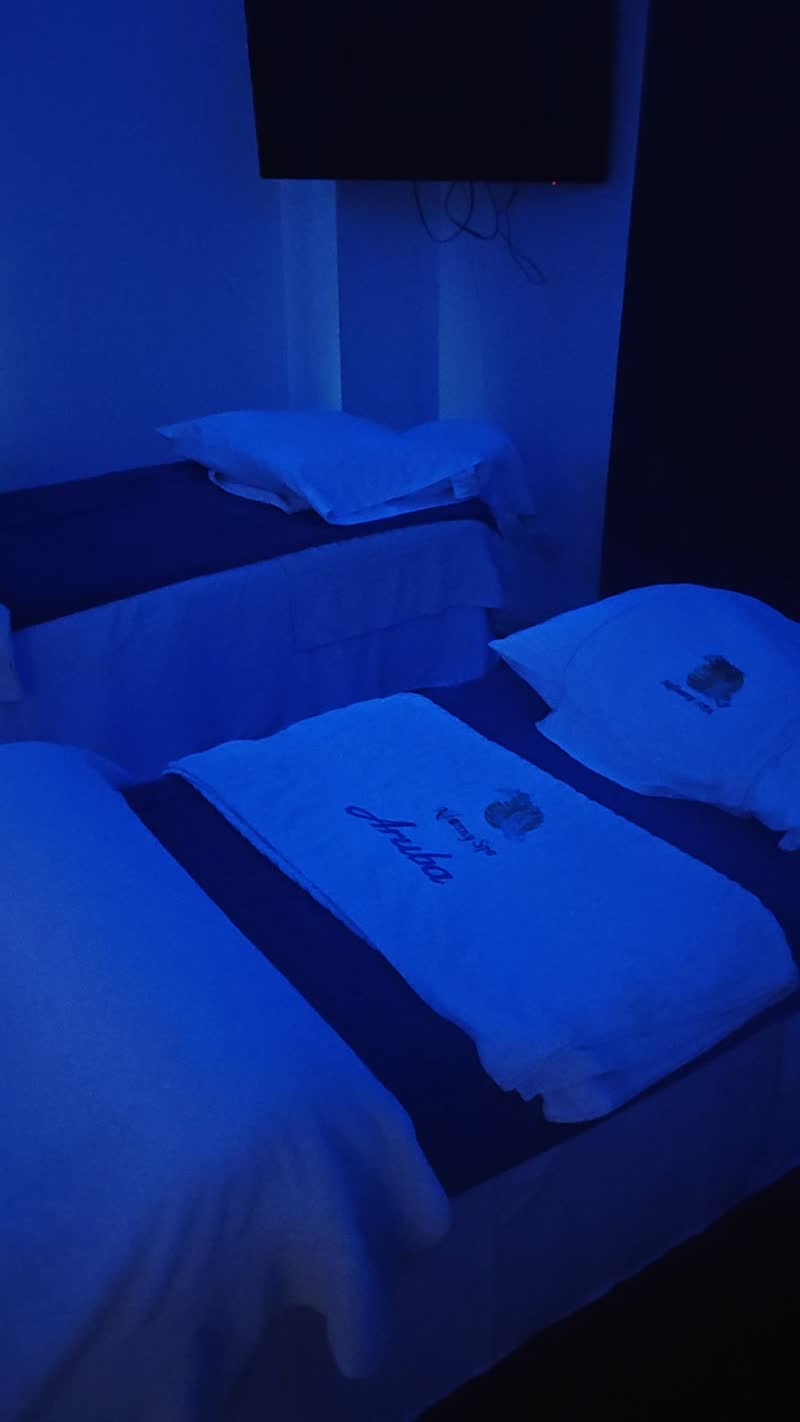 Massage tables made up with white towels bearing the Nafanny Spa name, in a room lit with blue light
